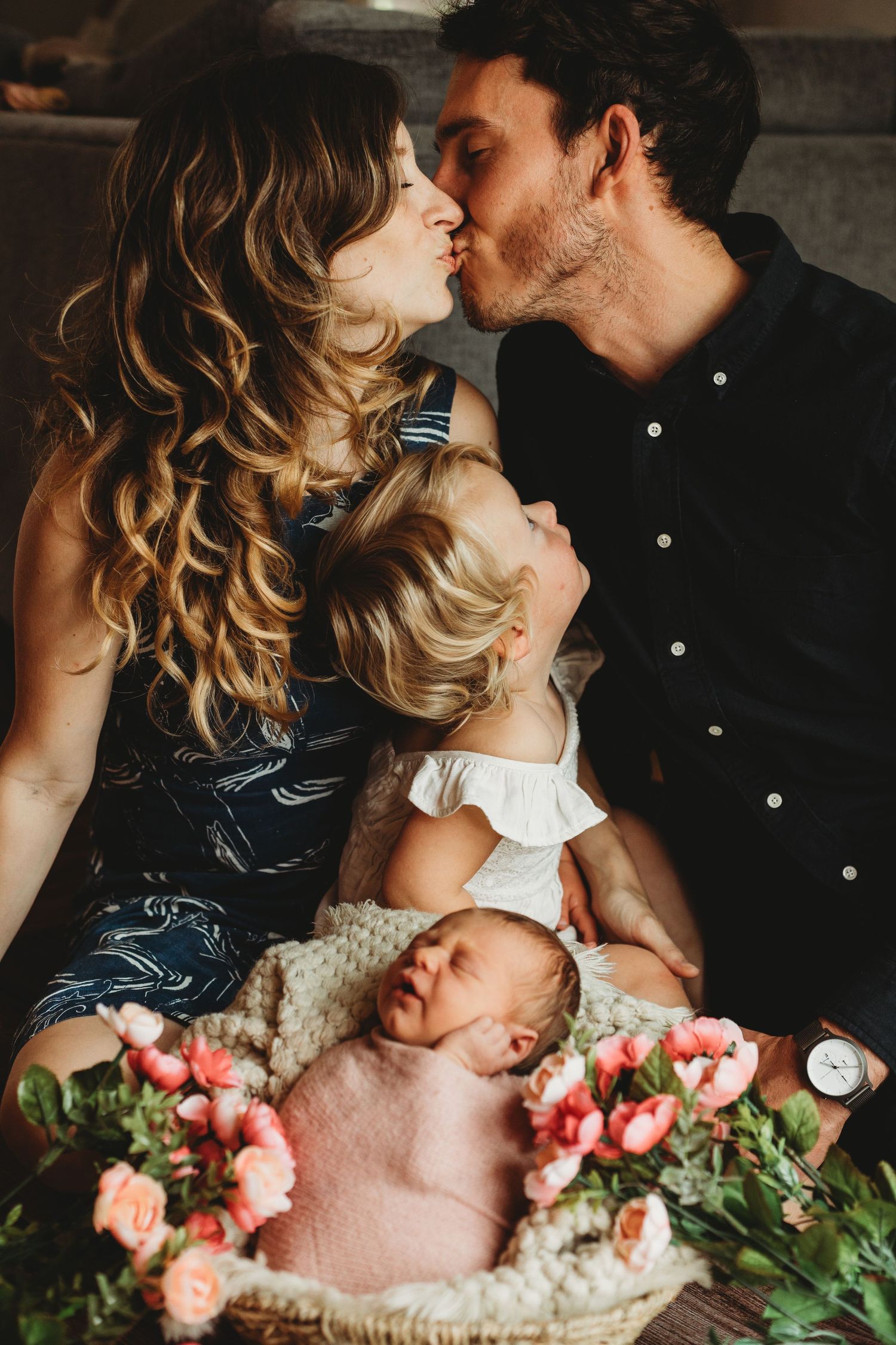 Tender family moment with sleeping newborn surrounded by pink roses in dim lighting. Annapolis newborn photographer