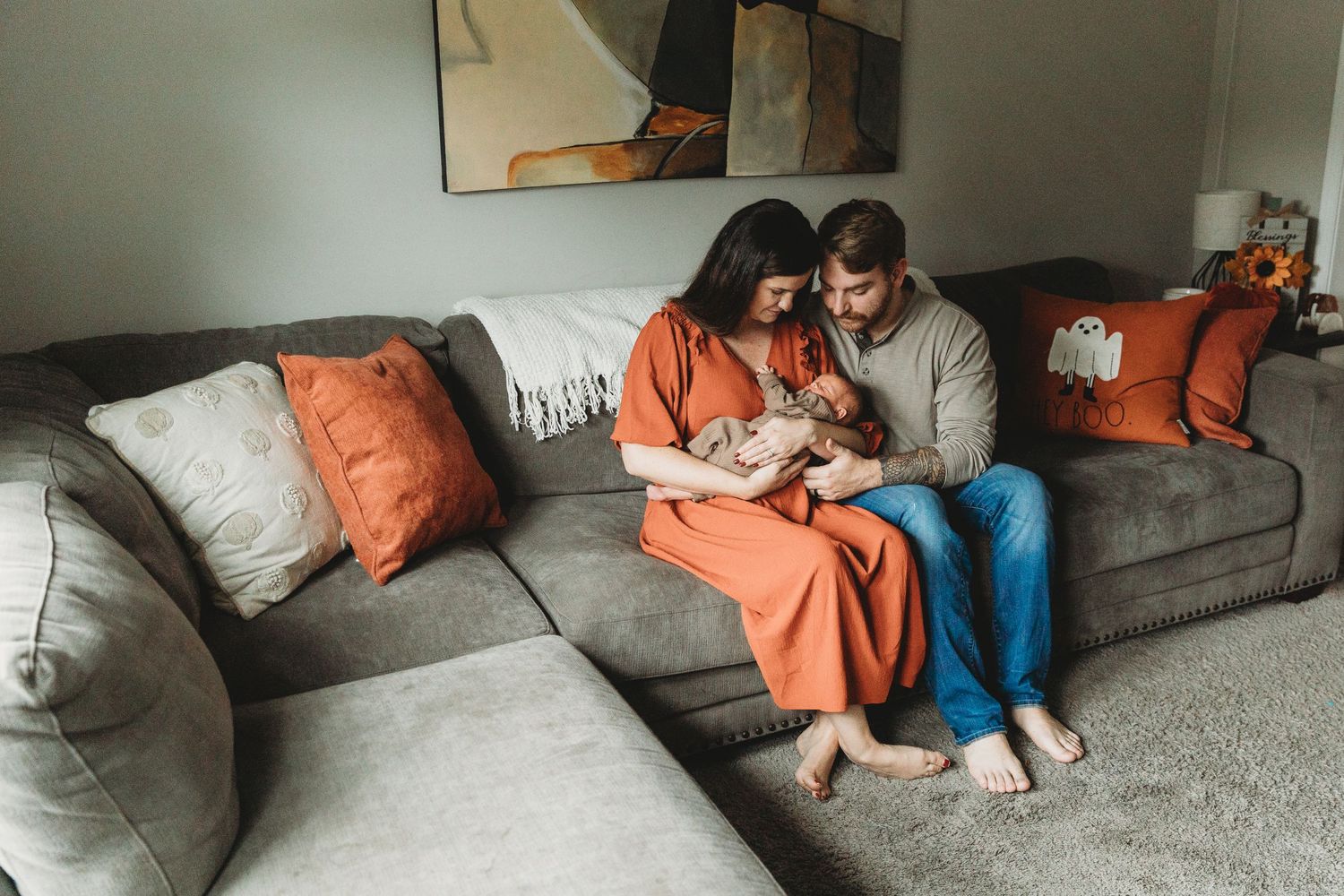 A couple sits together on a gray sectional sofa in a cozy living room. Maryland Newborn photographer. Annapolis newborn photographer
