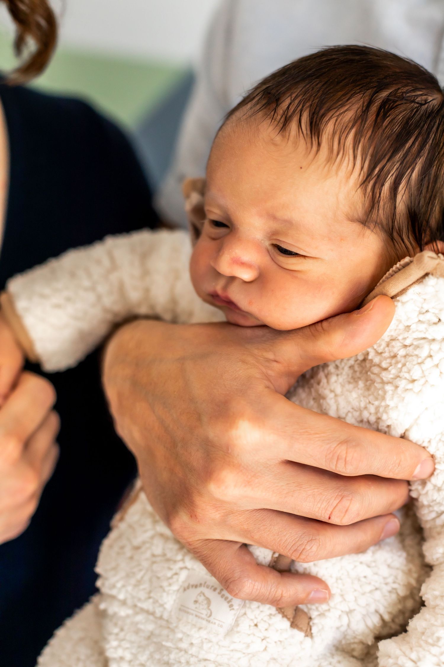 Delicate hands cradle a sleeping newborn wrapped in soft white fabric.