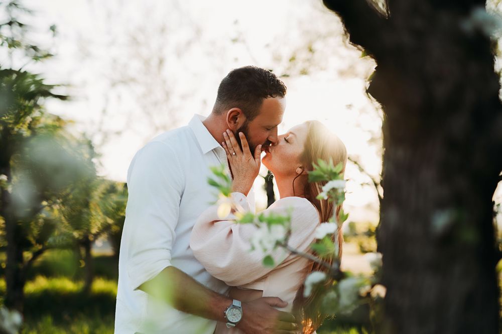 Romantic couple shares tender kisses in a sunlit garden setting during a golden hour photo session.