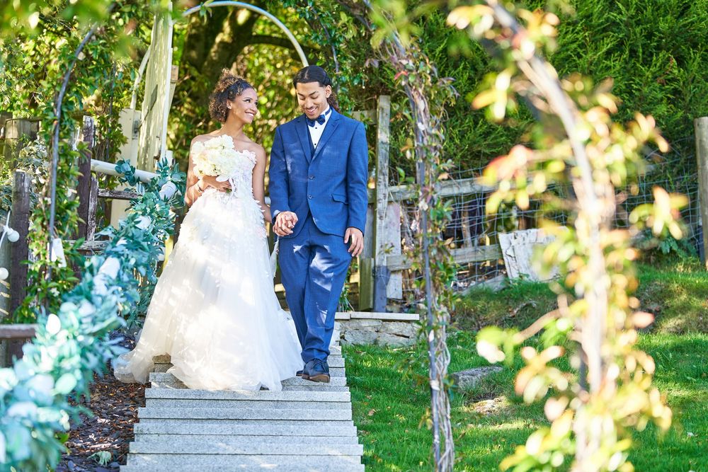Wedding couple walks through a lush garden pathway under natural sunlight.