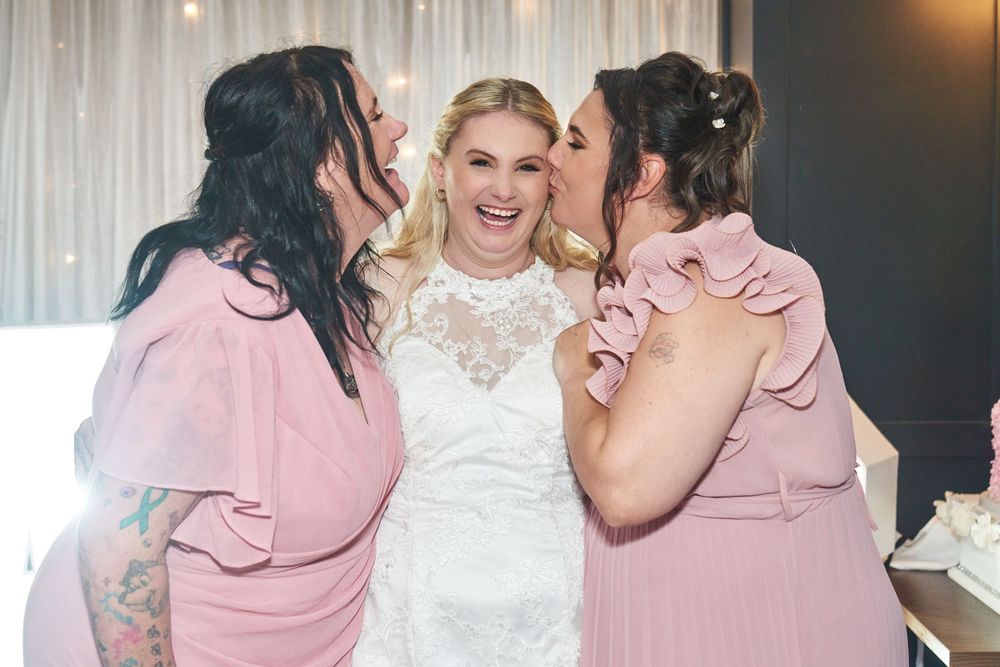 Bridesmaids in pink dresses share joyful moments with bride in white lace gown during wedding celebration.