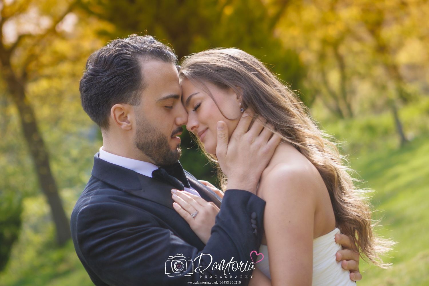 A wedding couple sits together on a bench in a lush garden setting.