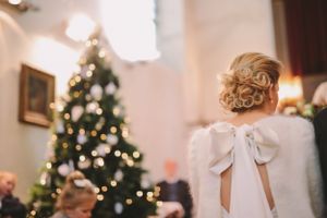 A Christmas tree glows with lights behind a white dress with a large bow detail.