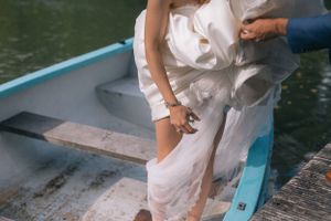 Person in flowing white dress climbing into blue rowboat at waters edge.