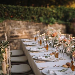 An elegant outdoor table setting with floral centerpieces and place settings against a stone wall.