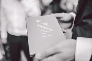 Black and white close-up of hands holding vows during a wedding ceremony.