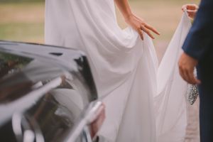 Close-up view of hands adjusting flowing white wedding dress fabric during an outdoor ceremony.