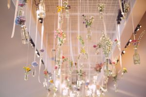 Decorative glass bottles with flowers hang from ceiling on strings creating whimsical display.