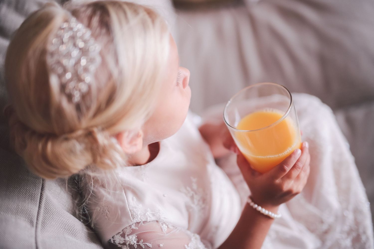 Person holding orange juice glass wearing white lace dress with elegant updo hairstyle.