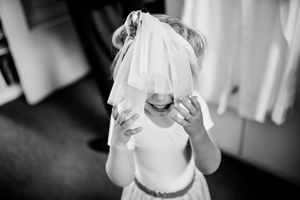 A wedding veil drapes over a bride covered in delicate white lace as she holds her hands to her face.