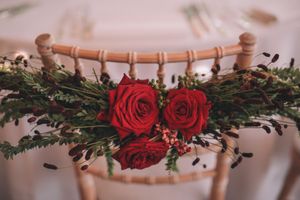 Red roses and greenery decorate a wooden chair back for an elegant wedding or event setting.