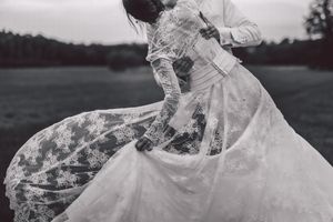 A flowing lace wedding dress twirls dramatically in black and white against a natural outdoor backdrop.
