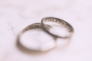 Two silver wedding bands with engraved text inside rest on a soft white textured surface in a romantic close-up shot.