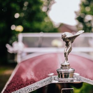 Classic Rolls-Royce Spirit of Ecstasy hood ornament against a red car with bokeh background.