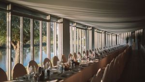 Elegant long dining table setup by windows overlooking natural scenery.