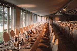 Long dining table with elegant place settings arranged in a room with floor-to-ceiling windows and soft lighting.