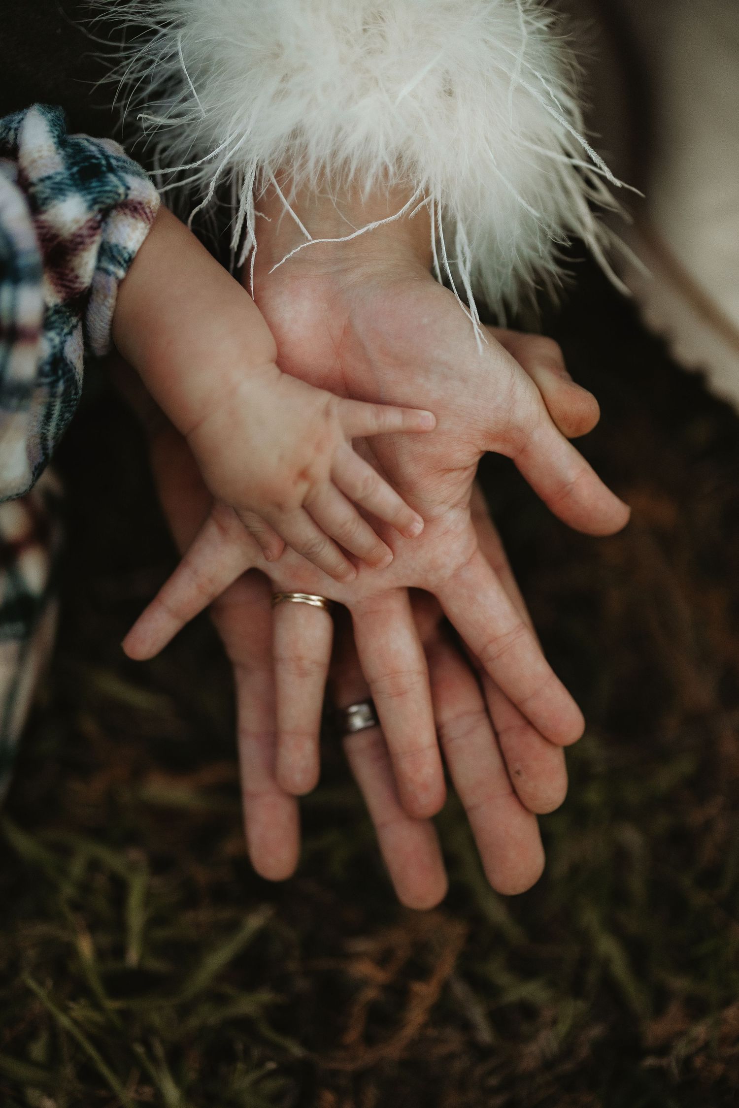 Three hands stacked together showing wedding rings and white feather.