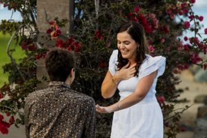 A couple poses together against a backdrop of vibrant red flowering bushes.Shot By Zeus Holbrook San Diego Wedding Photographer