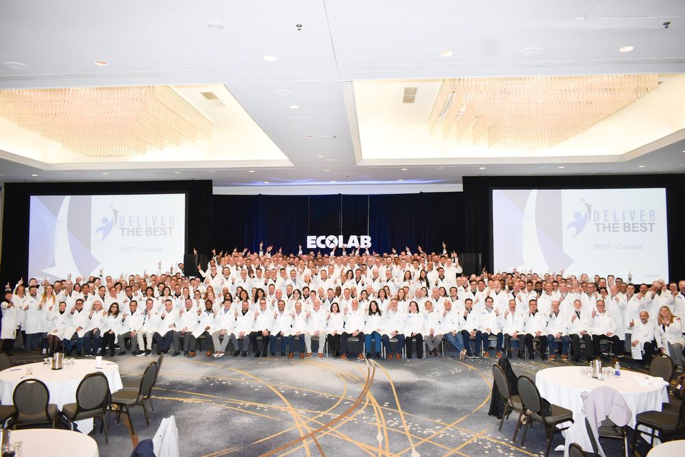 Large Ecolab corporate event with hundreds of employees in white shirts gathered in a ballroom for a company conference.
