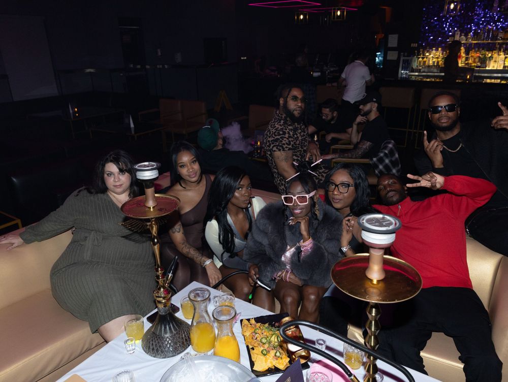 Friends gather around hookah pipes and drinks at dimly lit lounge booth.