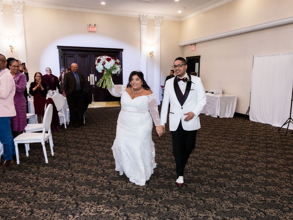 Newlyweds walk down the aisle together in wedding attire across patterned carpet at reception venue.