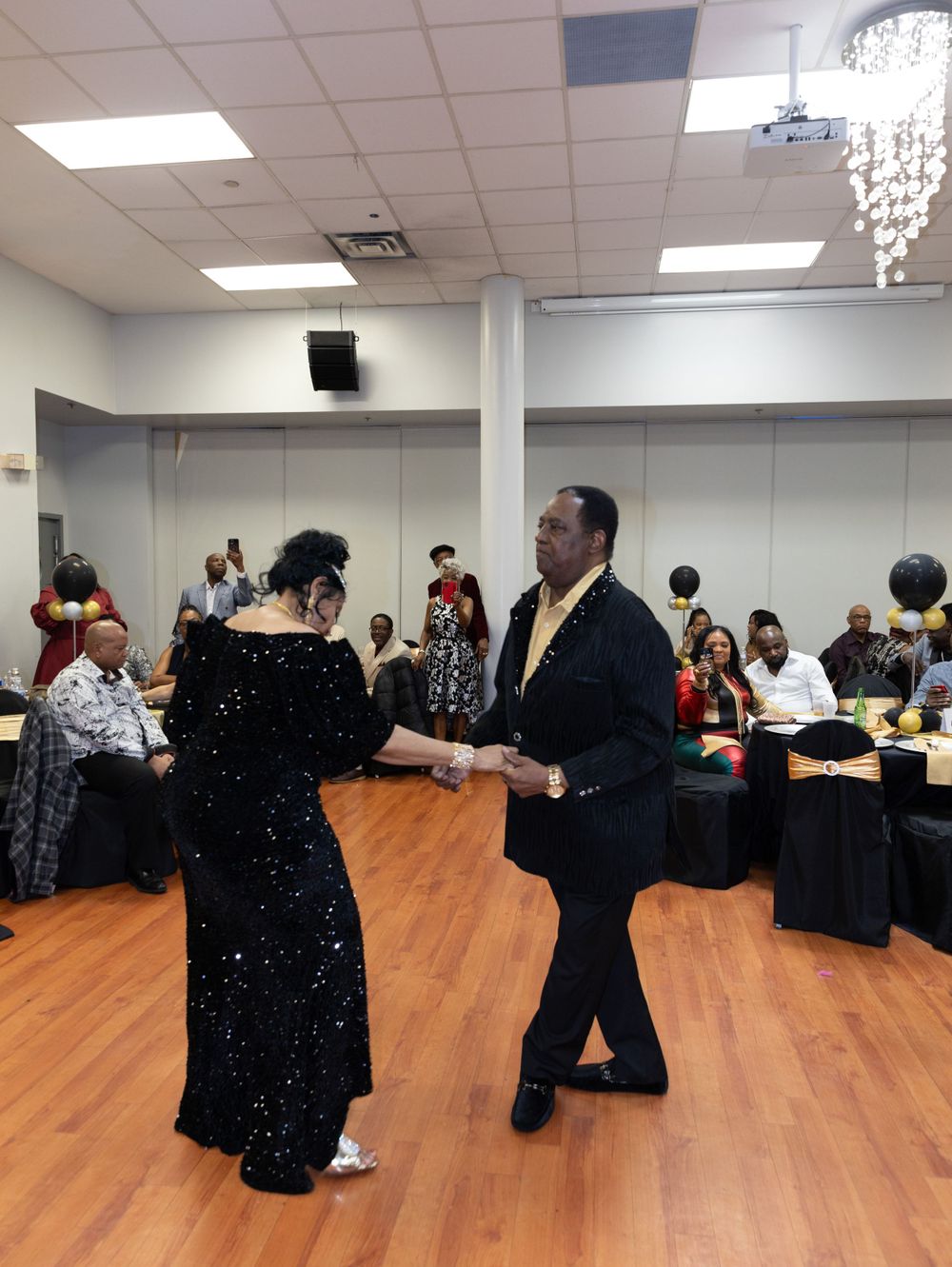 Couple dancing at formal event in room decorated with black and gold theme.