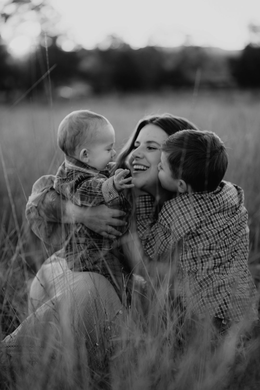 A heartwarming black and white photograph of a family sharing joyful moments together in a tall grass field.