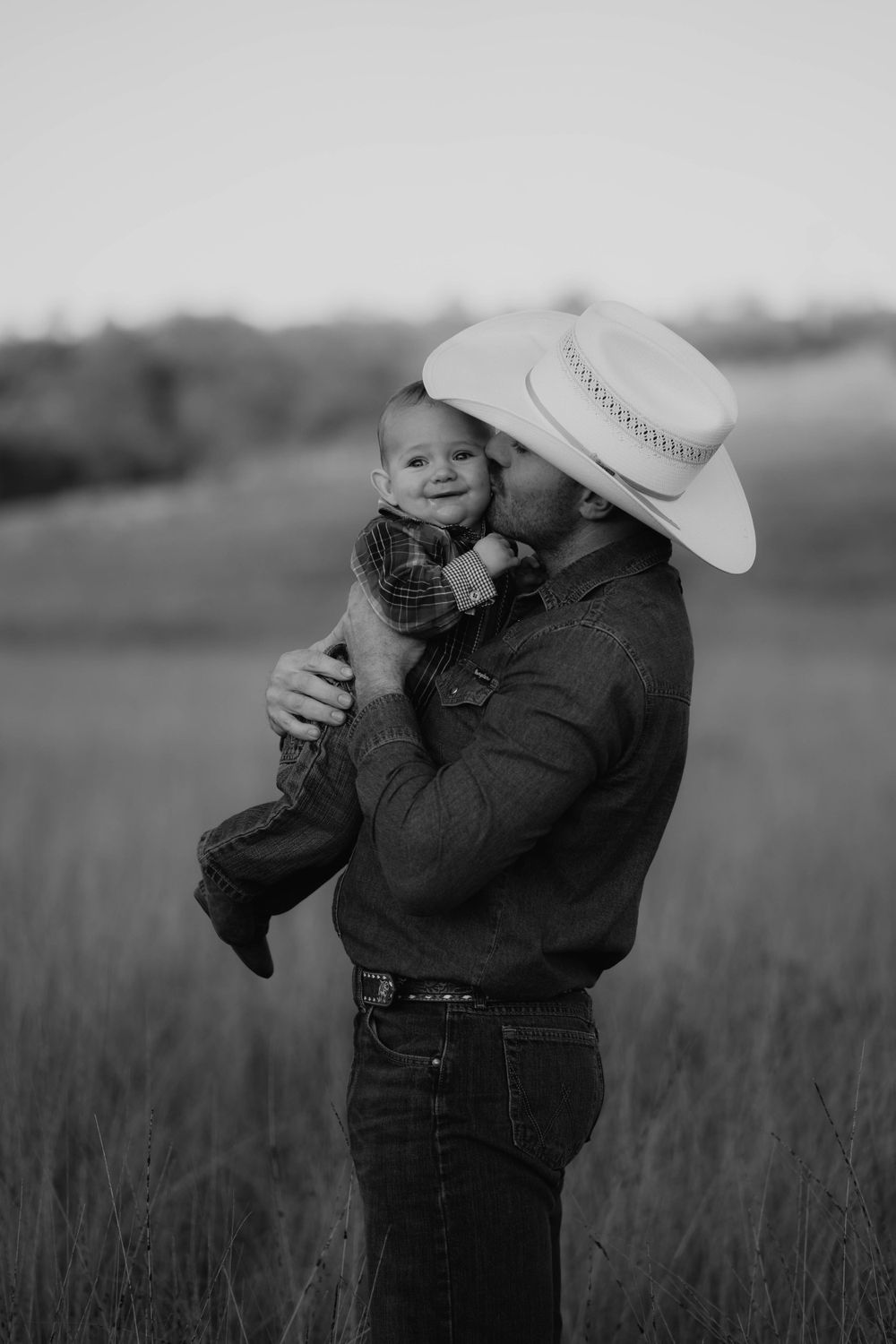 Black and white portrait of a tender moment between parent and child in a grassy field.