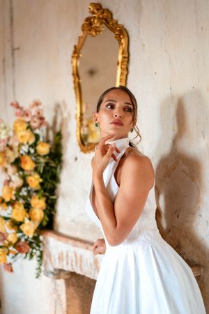 Artistic bridal portrait with white gown against vintage wall with floral decorations.