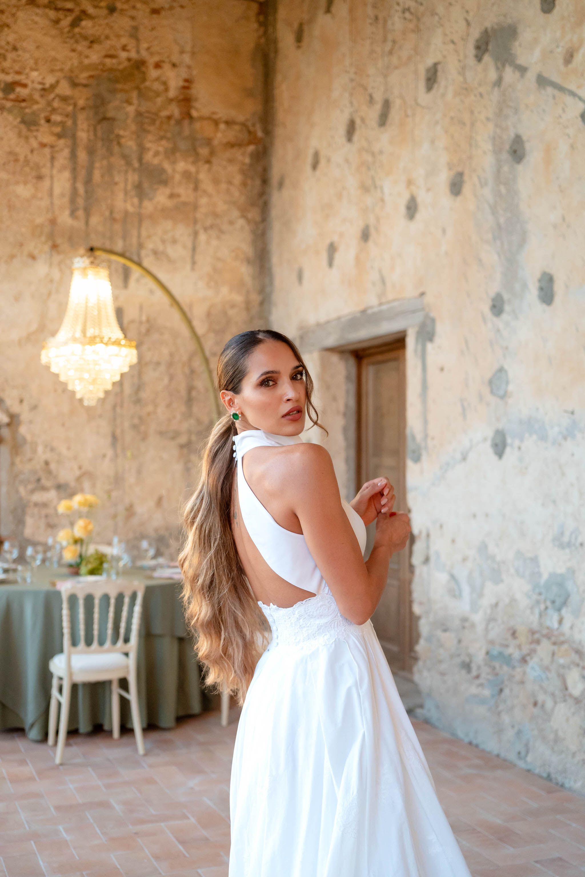 A person in a white dress twirls playfully in a rustic room with weathered walls and a chandelier.