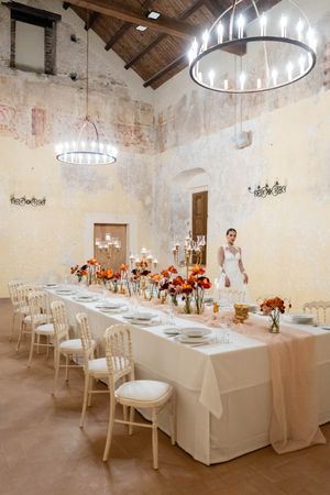 Long white dining table set with elegant place settings under rustic wooden beams and crystal chandeliers.