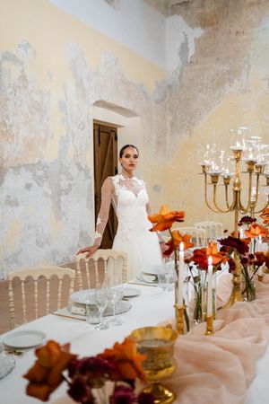 Wedding reception table decorated with orange flowers and gold candelabras against weathered walls.