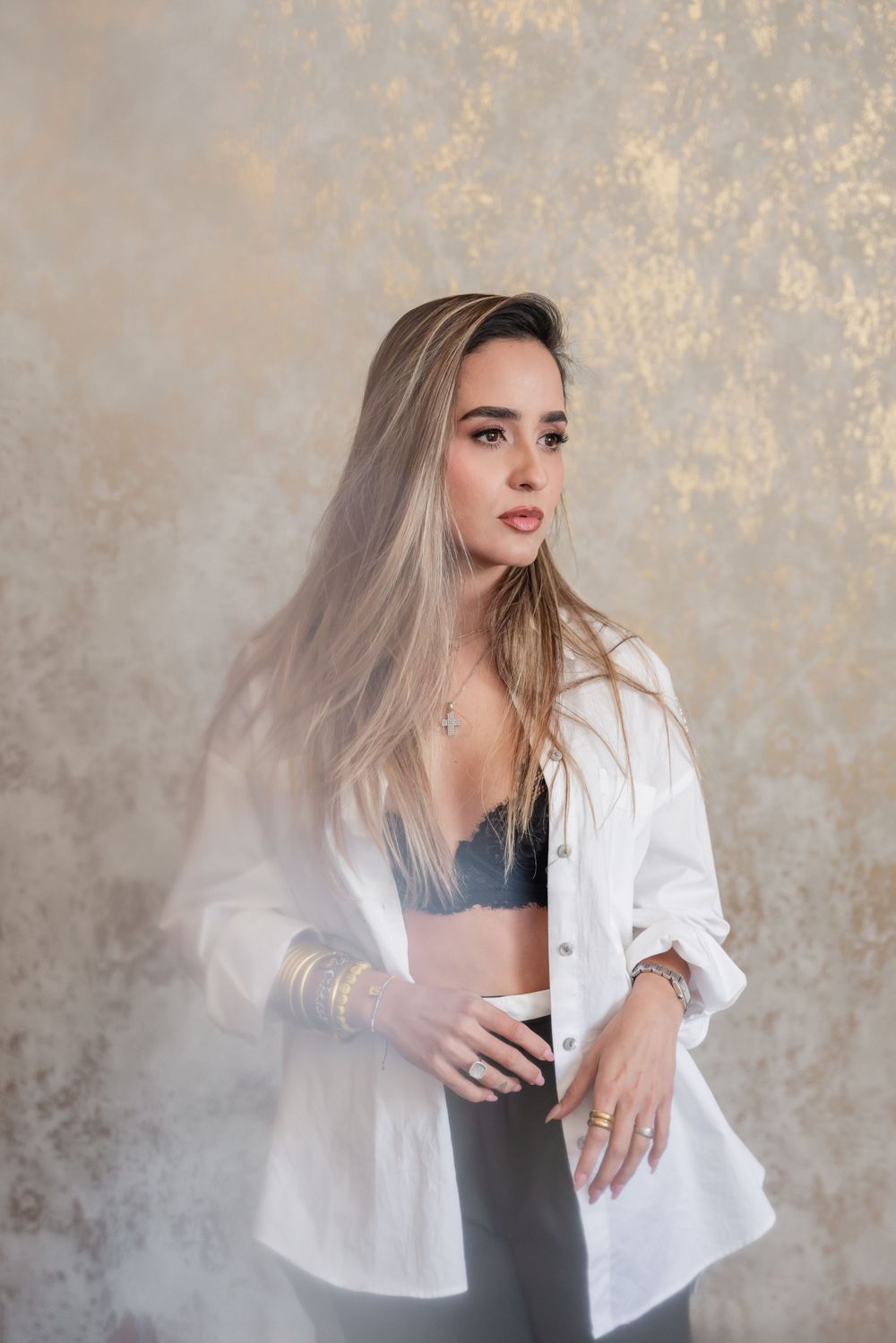 Fashion portrait of woman in white button-up shirt and dark top against textured backdrop with dramatic lighting.