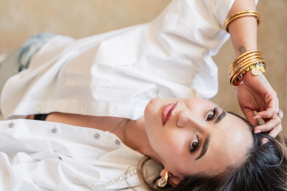 Artistic portrait of woman lying down wearing white shirt and gold bracelets.