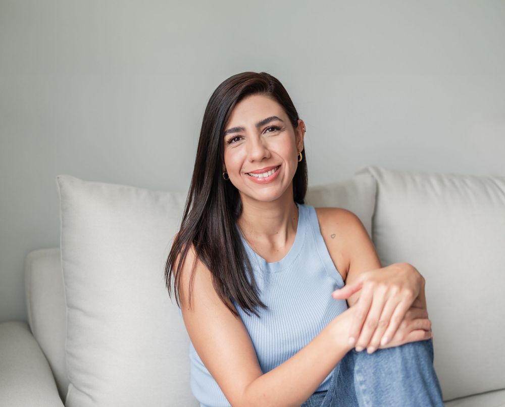 Casual portrait of woman in blue tank top sitting on light colored couch.