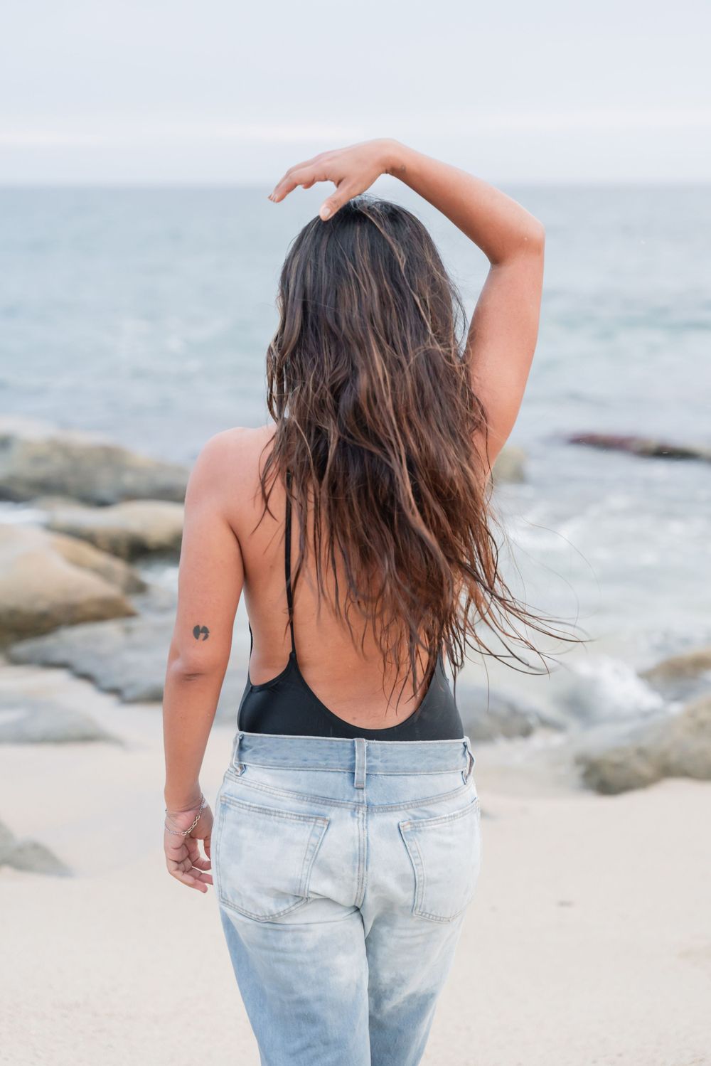 Back view showing long dark hair blowing in ocean breeze.