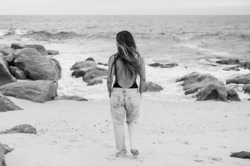 Black and white beach scene with person walking towards rocky ocean vista.