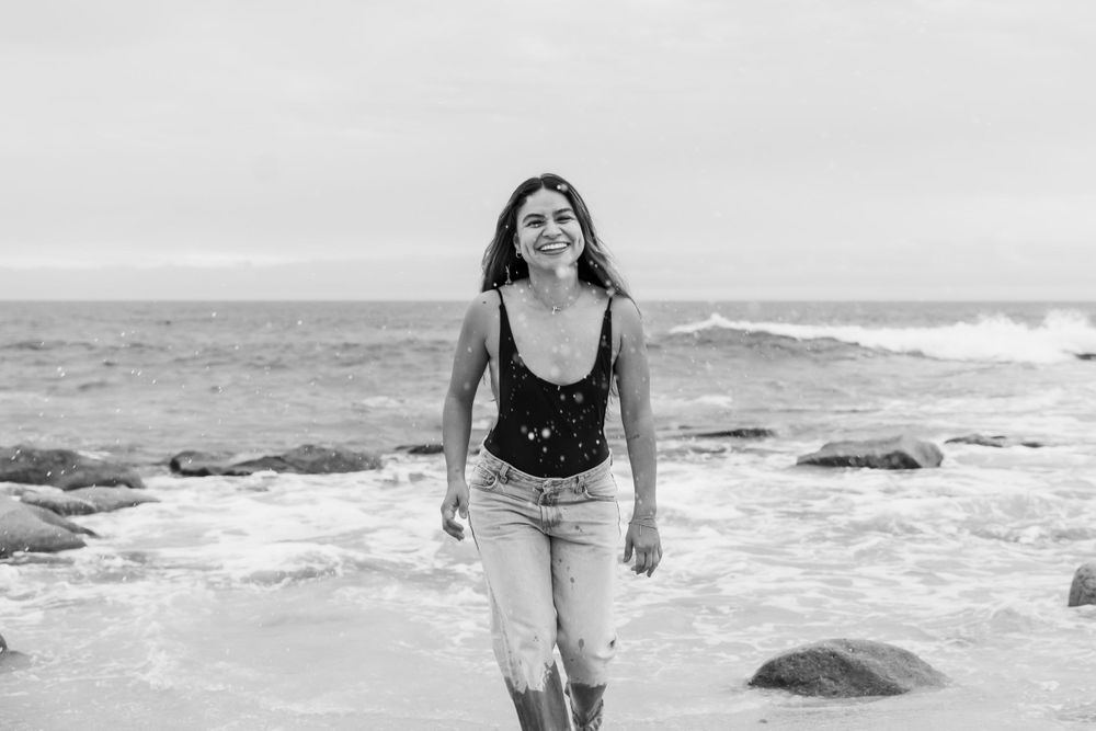 Black and white photo on rocky beach with waves in background.