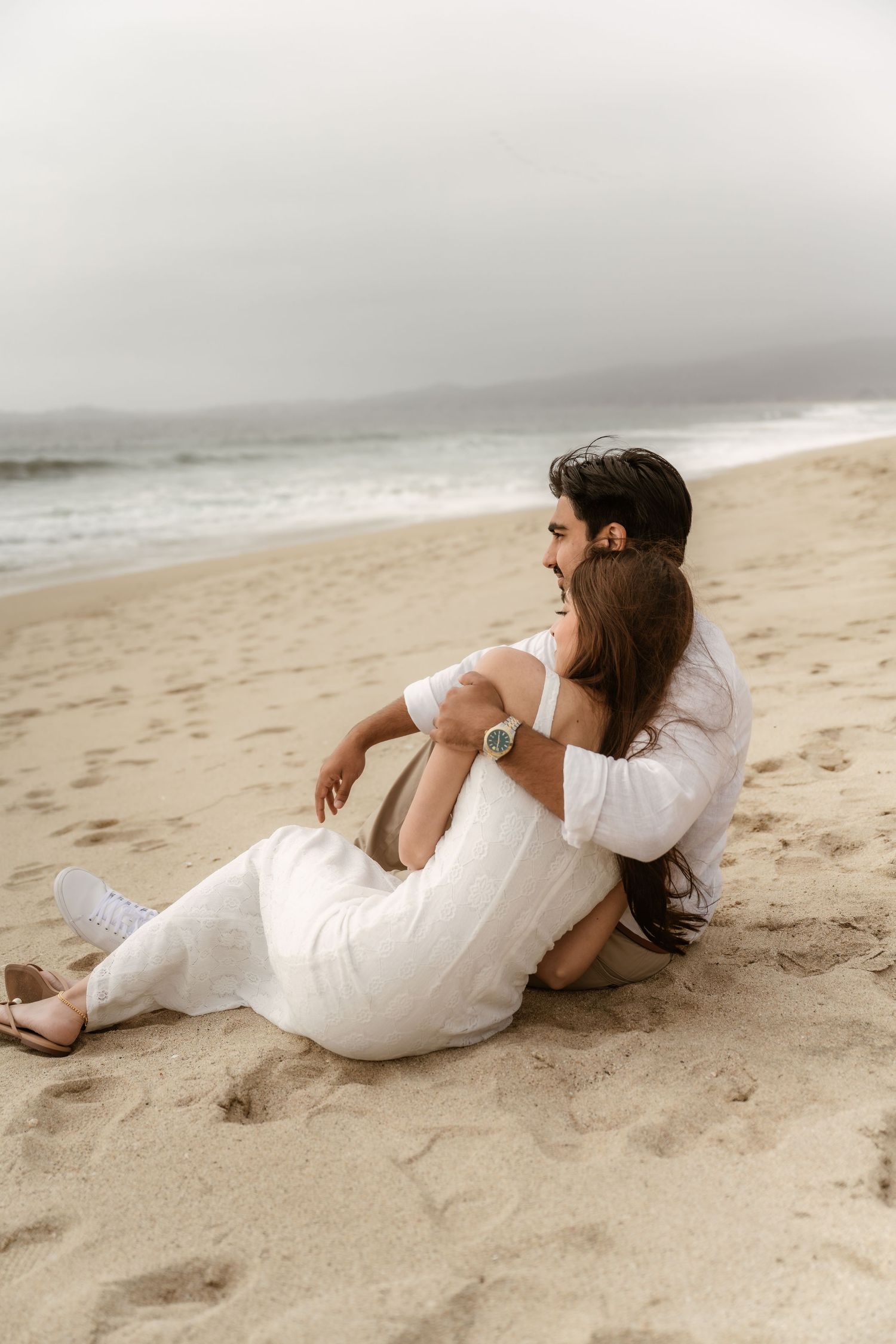 Romantic couple in white clothing posing on sandy beach at sunset.