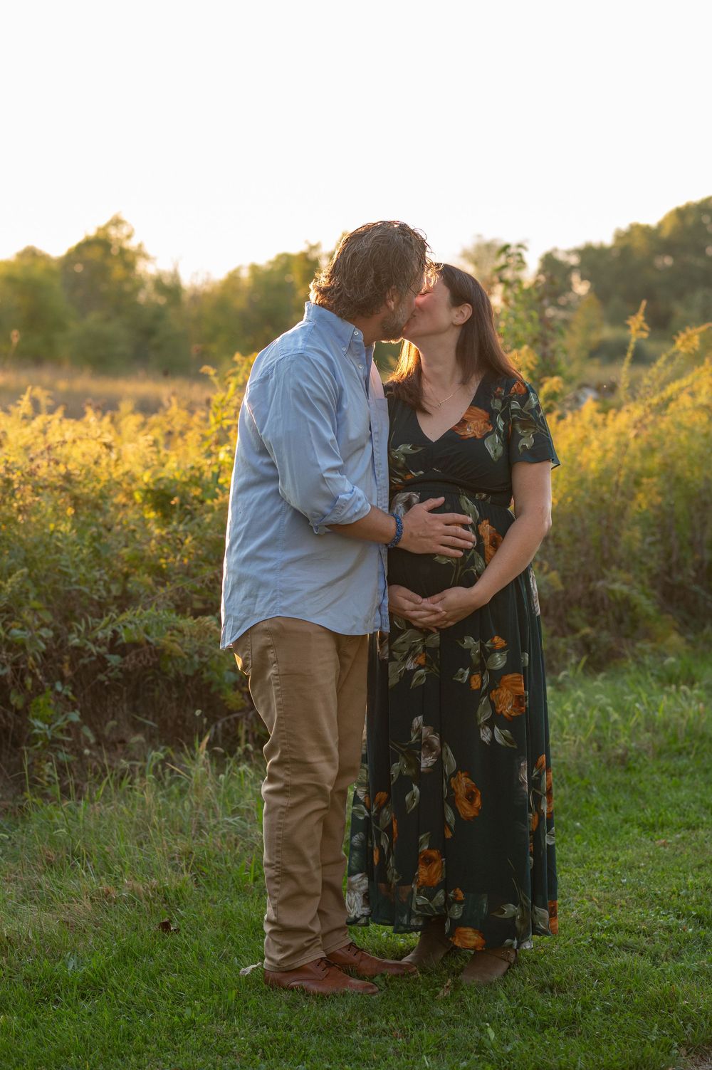 Expecting couple kisses while cradling baby bump during golden hour maternity session outdoors.