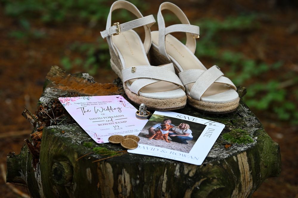 Wedding shoes and invitation displayed on tree stump with engagement photo for wedding detail shot.