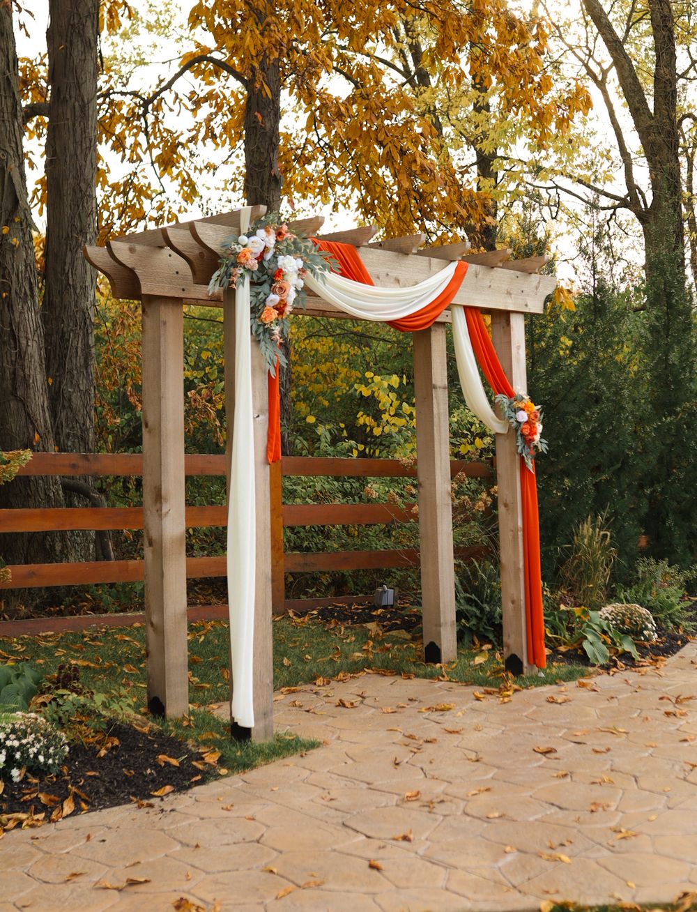 Rustic wooden wedding arch decorated with orange and white fabric draping and floral accents in autumn.