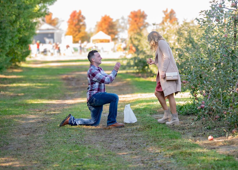 Man proposing on one knee to his girlfriend in an apple orchard on a sunny autumn day.