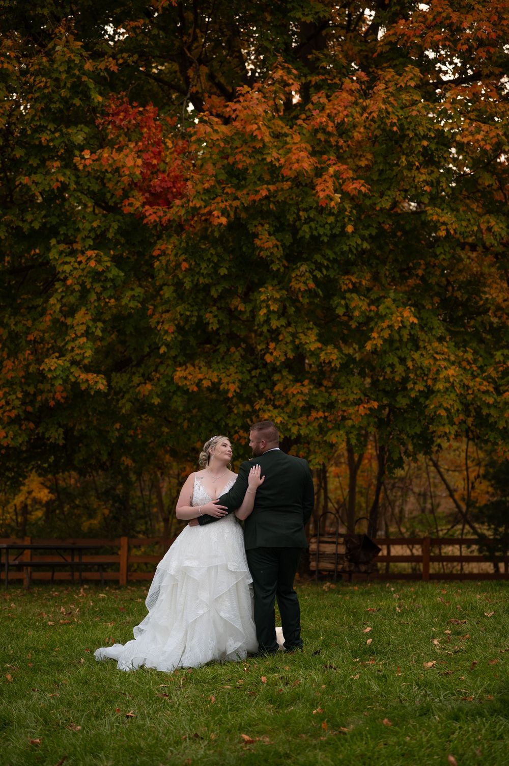 Bride and groom sharing a romantic moment beneath a vibrant red and orange autumn tree outdoors.