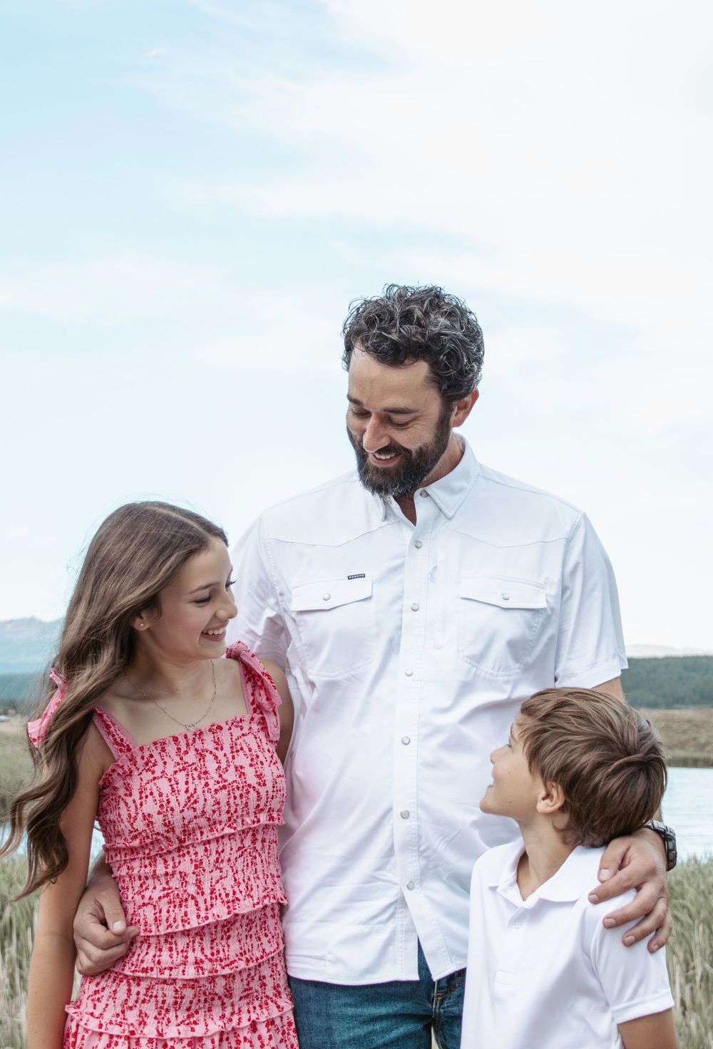 Family in casual attire shares candid moments together outdoors against a scenic mountain backdrop.