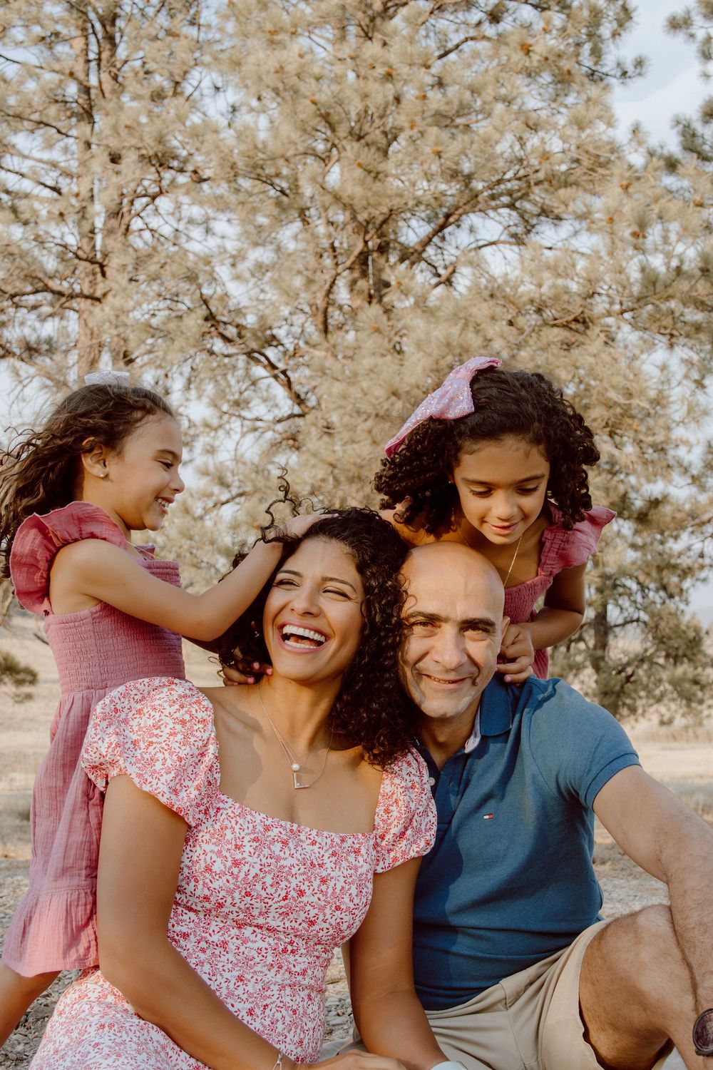 A joyful family moment captured outdoors with natural sunlight and trees in the background.