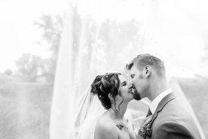 A loving couple shares a romantic kiss on their wedding day in a soft black and white portrait.