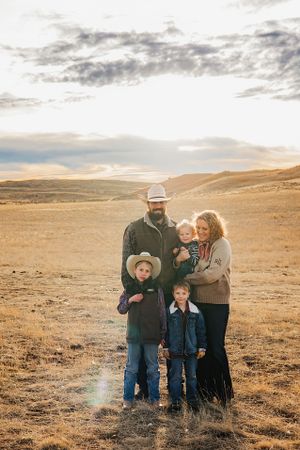Family stands together on a golden prairie landscape at sunset with rolling hills and cloudy sky in the background.