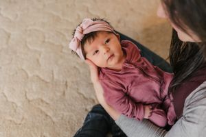 A small baby in a mauve outfit and headband is cradled lovingly.